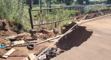 A crumbling bridge is pictured being cordoned off with danger tape. fields and trees are seen in the background.
