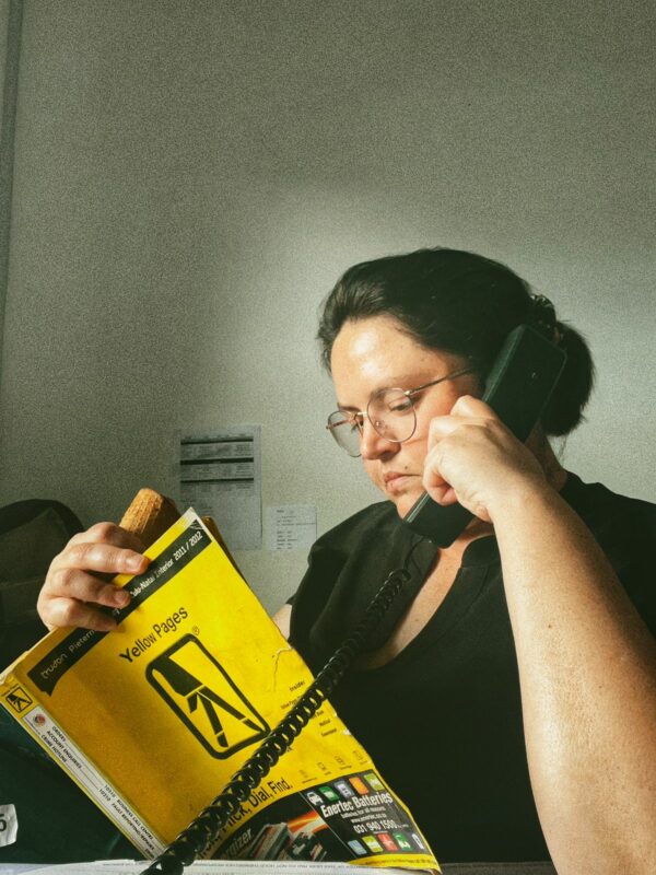 A journalist is looking at the phone book with ice cream in the one hand and the telephone receiver pressed against her ear.