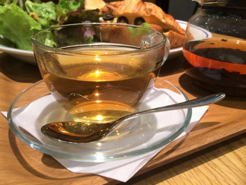 A cup of Earl Grey tea in a glass tea cup in a glass saucer with a teaspoon next to it. It is on top of of a white napkin. All the items are on a wooden table.