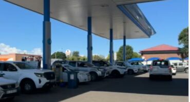 Several cars photographed at a fuel station waiting to fill their tanks.