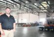 A photo of a business owner standing inside his workshop filled with heavy machinery tools.