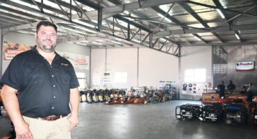 A photo of a business owner standing inside his workshop filled with heavy machinery tools.