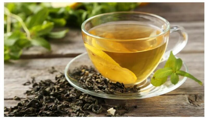 A cup of green tea in a saucer with dried tea leaves next to it.