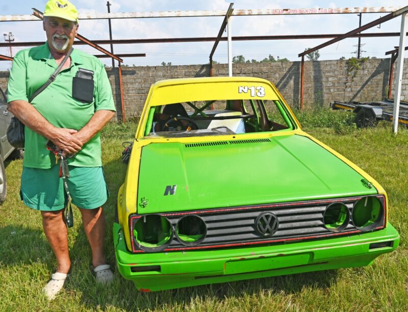 A green oval track track car is pictured with its driver next to it.