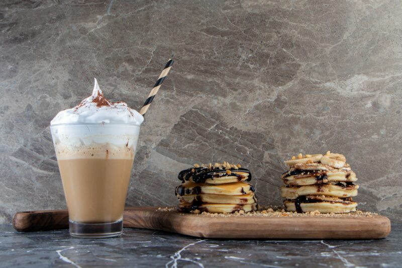 Pancakes with banana and chocolate topping on wooden board with delicious coffee.