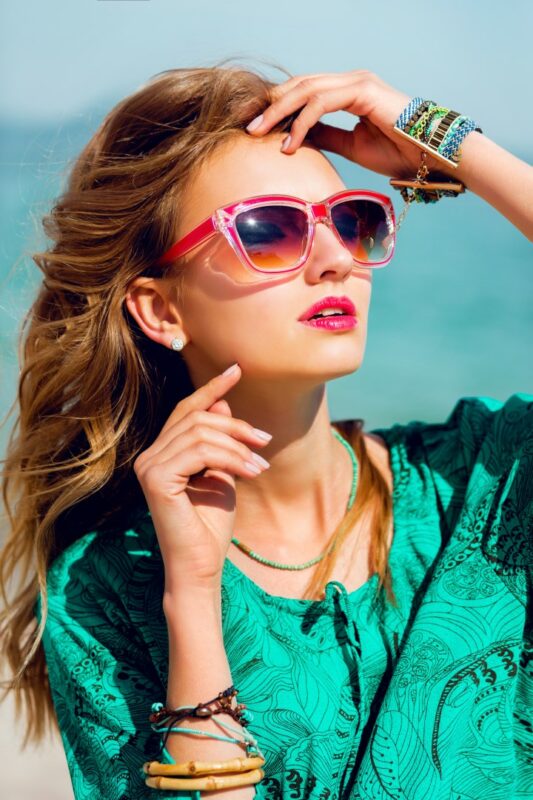 Stunning colorful outdoor summer portrait of pretty young blonde beautiful woman in cool sunglasses posing on the sunny tropical beach.