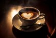 A overview photo of a cup of coffee on a wooden table in a dark light setting with a heart created with the milk.