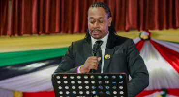 Mayor Dube in suit speaks at podium with microphone