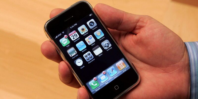 The first iPhone. A man is holding the phone in his hand. The screen with all the applications is visible.