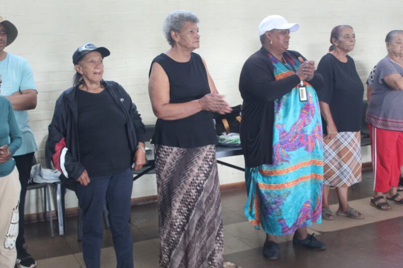 A group of women are photographed dancing inside a community hall.