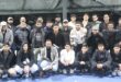 A large group of padel players are photographed on a padel court at night.