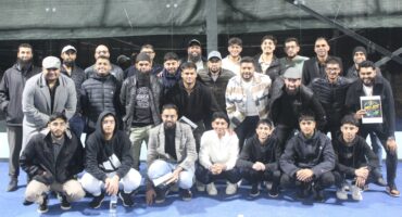 A large group of padel players are photographed on a padel court at night.