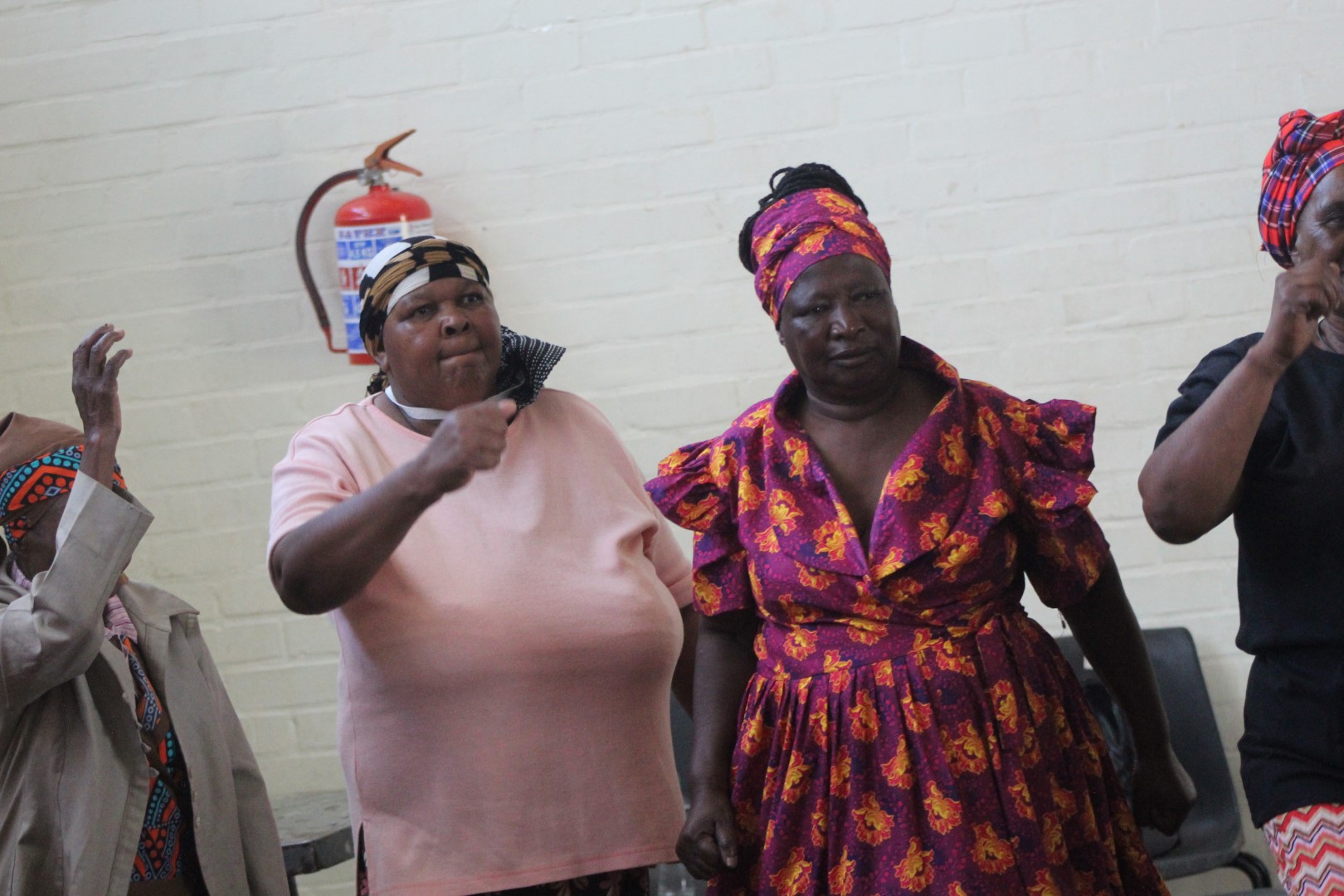 A group of women are photographed dancing inside a community hall.