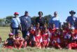 A group of soccer players and event organisers pose for a photo on the soccer field outside in the sun.