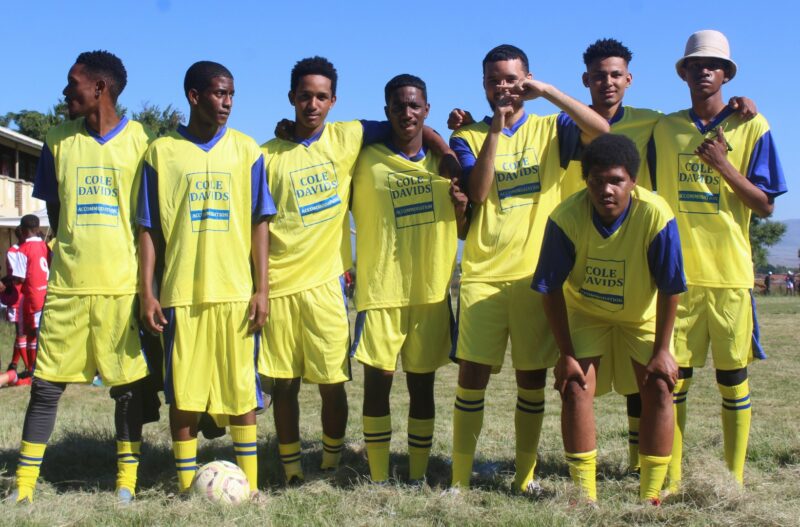 A group of soccer players dressed in yellow and blue sports attire pose for a photo.