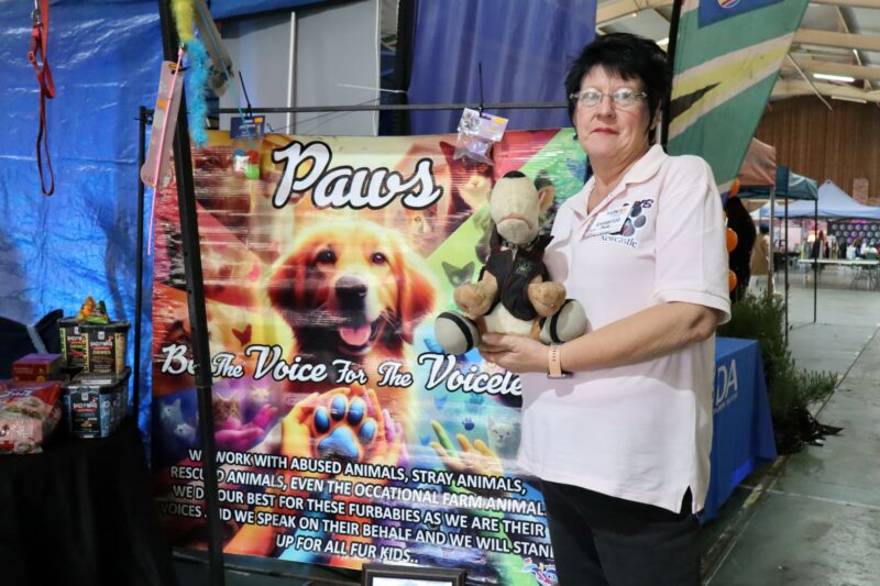 A woman holding a teddy poses in front of her PAWS banner.