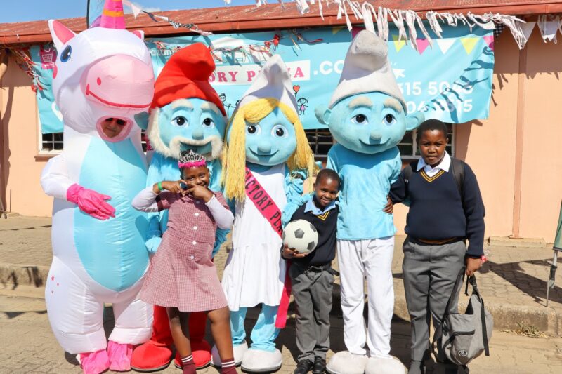 three children are photographed with smurfs and unicorn mascots at a festival.