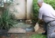 Man inspects overflowing sewage near residential drainage outlet
