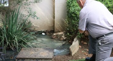 Man inspects overflowing sewage near residential drainage outlet
