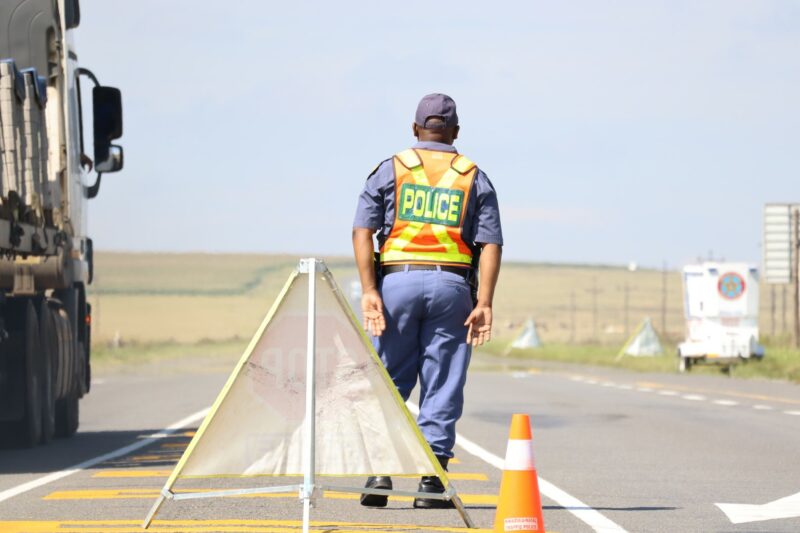 A South African Police Service offiver is standing on the tar road during a joint law enforcement roadblock operation.