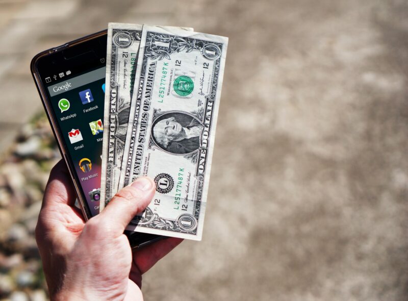 US Dollars and a cellphone in hand.