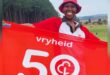 Image of a woman who completed her 50th parkrun, holding a banner.