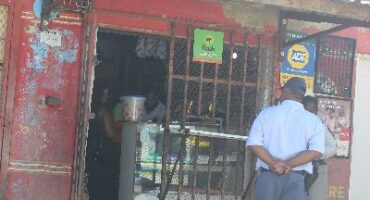 Photof of a SAPS officer in front of a shabby tuckshop type building in Glencoe, KZN.