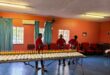 Three grown-ups wearing red is photographed packing out food parcels at a local orphanage.