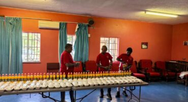 Three grown-ups wearing red is photographed packing out food parcels at a local orphanage.
