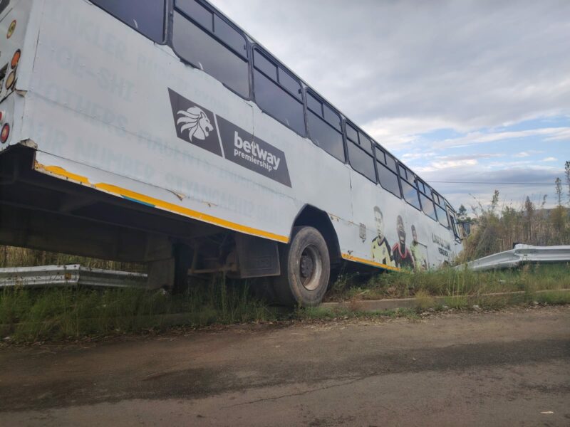 An image of a bus that crashed through a road barrier on the P38 Madadeni Road in Newcastle. You can see the bus hanging over the barrier in between trees.
