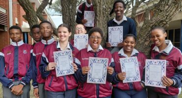 A group of scholars are photographed outside holding their certificates.