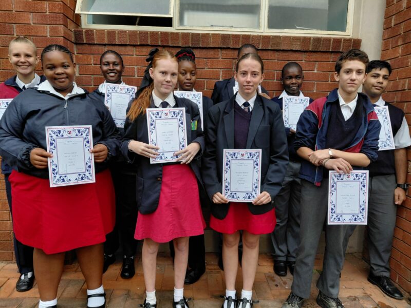 A group of scholars are photographed outside holding their certificates.