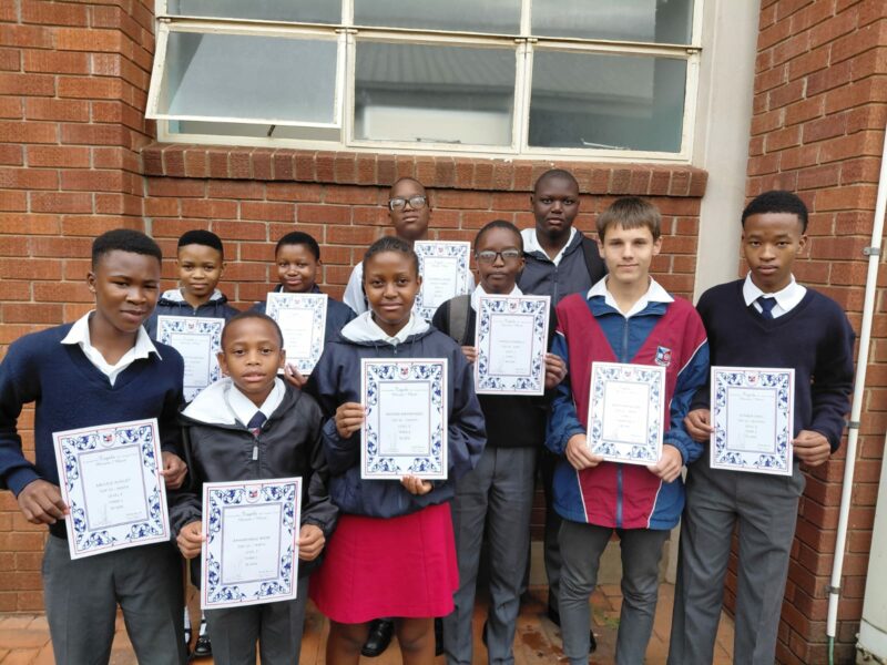 A group of scholars are photographed outside holding their certificates.