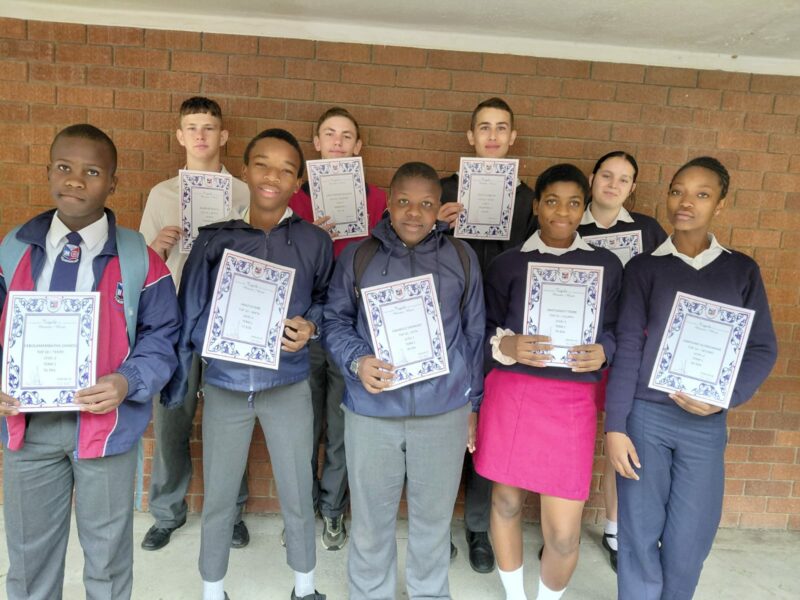 A group of scholars are photographed outside holding their certificates.