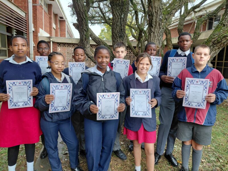 A group of scholars are photographed outside holding their certificates.