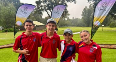 A photo taken of four young golfers posing in red attire on a golf coarse.