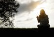 Sad and depressed woman sitting alone at the field during beautiful sunset with park background. Selective focus.
