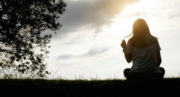 Sad and depressed woman sitting alone at the field during beautiful sunset with park background. Selective focus.