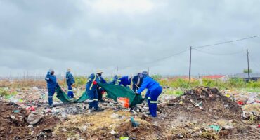 Several municipal workers dressed in blue overalls are pictured cleaning up an illegal dumping site.