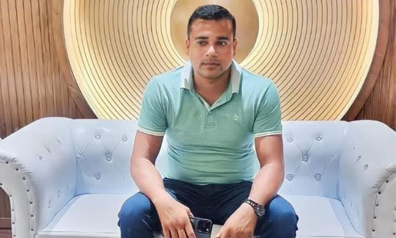 A photo taken of the late, Sumon Miah, posing on a couch in front of a gold background.