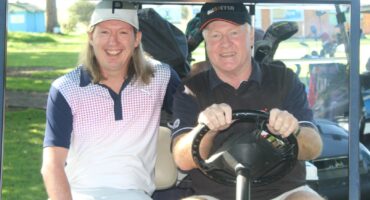 Two men are pictured on a golf cart during the annual Albatros Golf Day. Both men are wearing golf attires with golf clubs behind them.