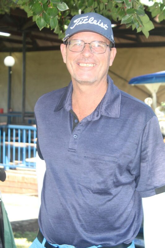 A golfer wearing a grey shirt and grey cap is photographed at a golf coarse.