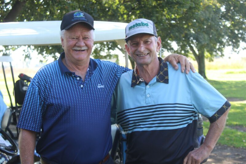 Two men are pictured on a golf cart during the annual Albatros Golf Day. Both men are wearing golf attires with golf clubs behind them.
