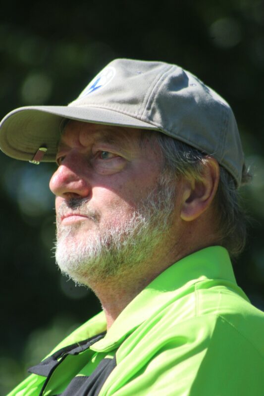 A golfer wearing a green shirt and grey cap is photographed on a golf coarse.