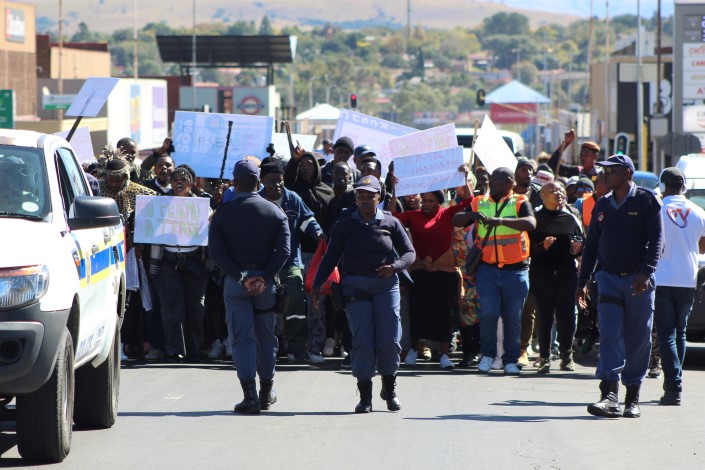 A large crowd of protestors branding signs are photographed walking through the streets of Newcastle, accompanied by policmen.