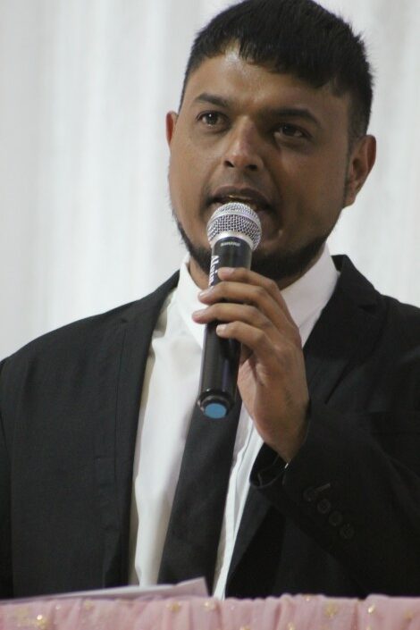 A portrait photo taken of a man in neat attire talking on a micrphone during a formal event.