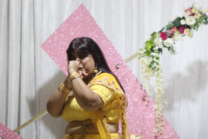 A photo of a woman dancing during a formal event in front of a white and pi nk backdrop.