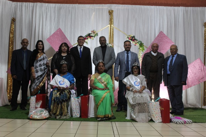 A group photo of people sitting and standing in front of a white and pink backdrop during a formal event.