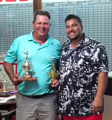 Two golfers are photographed in a club house holding a trophy.