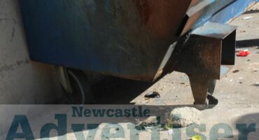 A photo taken of a blue municipal skip bin with a broken front wheel.